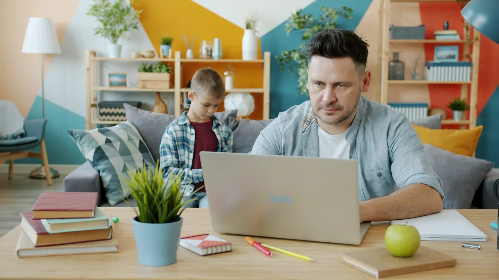Someone working at a laptop at home while a child uses a phone nearby